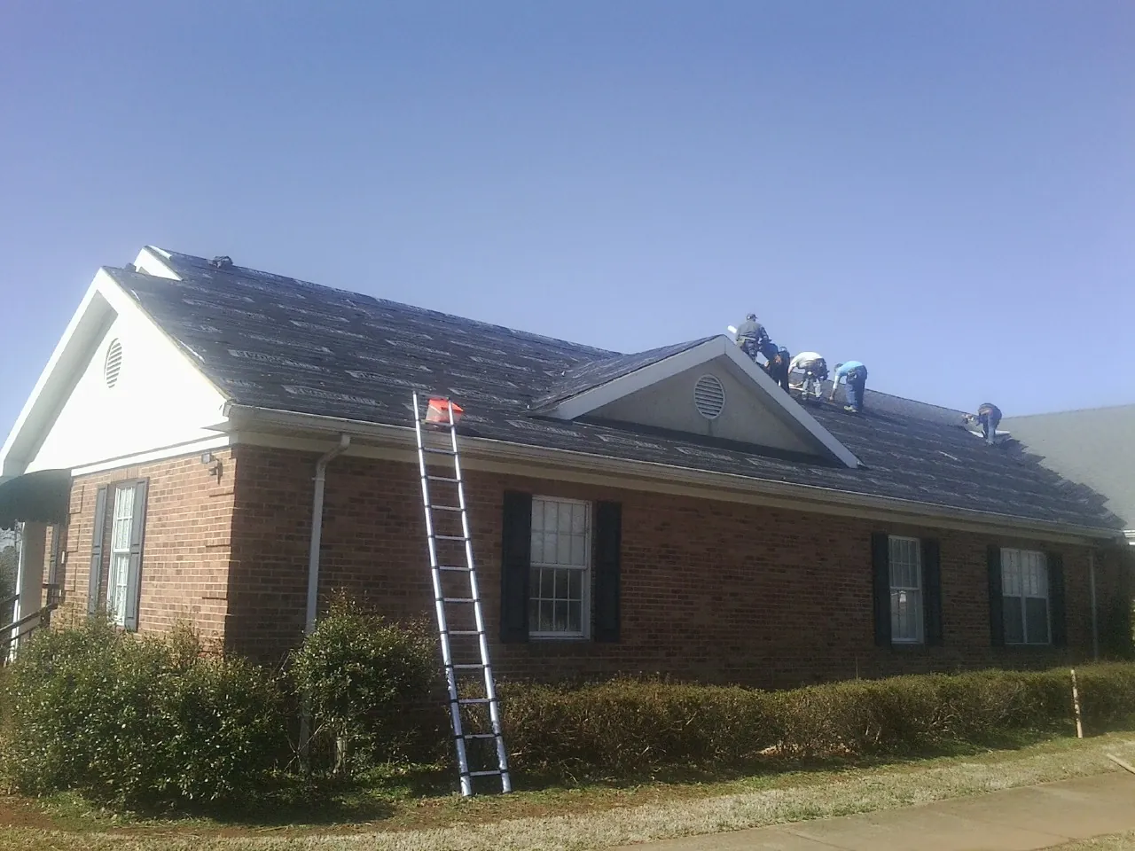 Crew tearing shingles off a brick ranch roof with a ladder set — Metal Roof Repair work by our crew in Kittery Point
