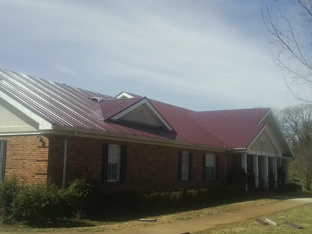 Red metal roof with gabled entries on a long brick building, from a Hail Damage Roof Repair job in Kittery Point