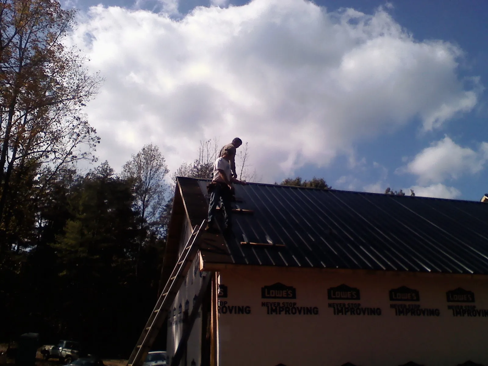 Roofer fastening dark metal panels high against a cloudy sky, from a Roof Inspection job in Kittery Point
