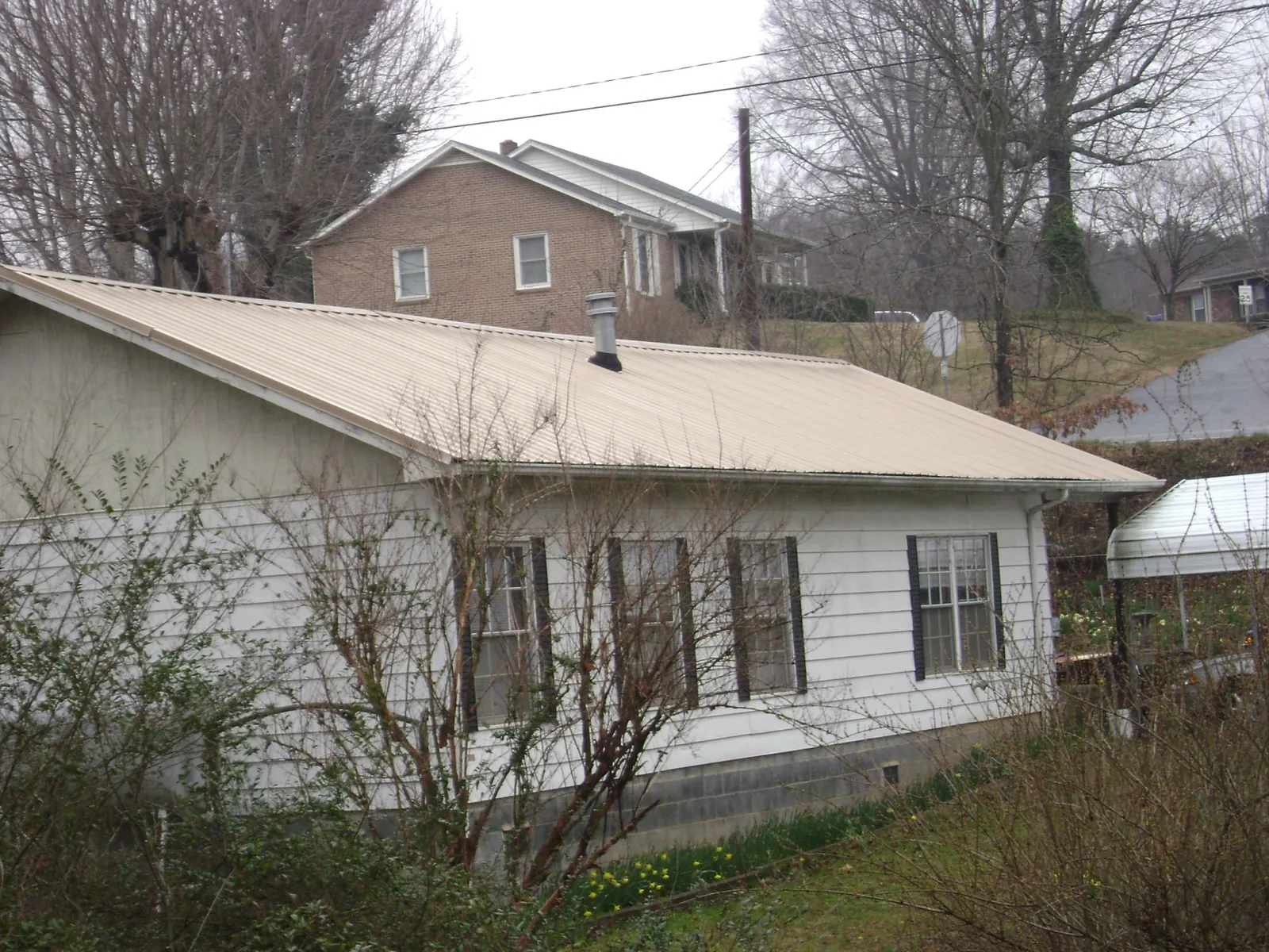 Tan metal roof on a white sided house set into a hillside — Commercial Roofing by Roofing Brothers in Kittery Point